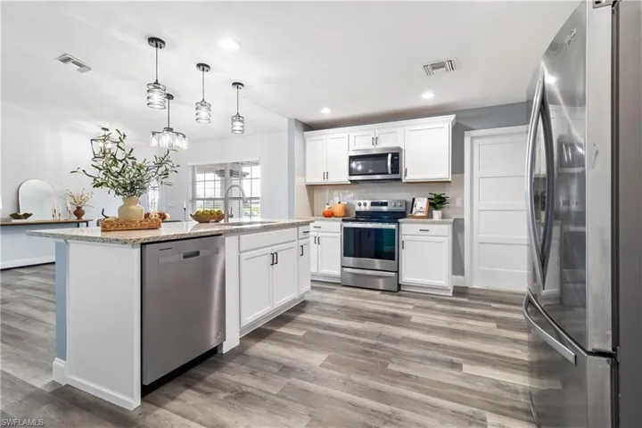 Kitchen with a sink, appliances with stainless steel finishes, light wood-style flooring, white cabinetry, and visible vents