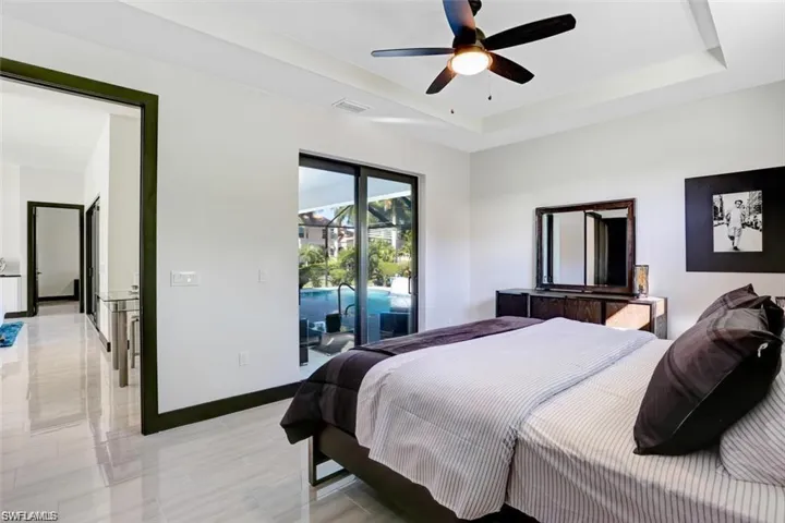 Bedroom with access to exterior, a tray ceiling, ceiling fan, and baseboards