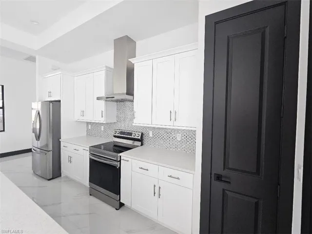 Kitchen featuring tasteful backsplash, white cabinets, marble finish floor, stainless steel appliances, and wall chimney range hood