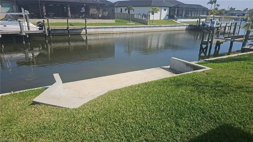 View of dock featuring a water view, boat lift, a residential view, and a lawn