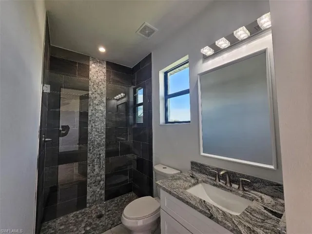 Bathroom featuring toilet, a shower stall, visible vents, and vanity