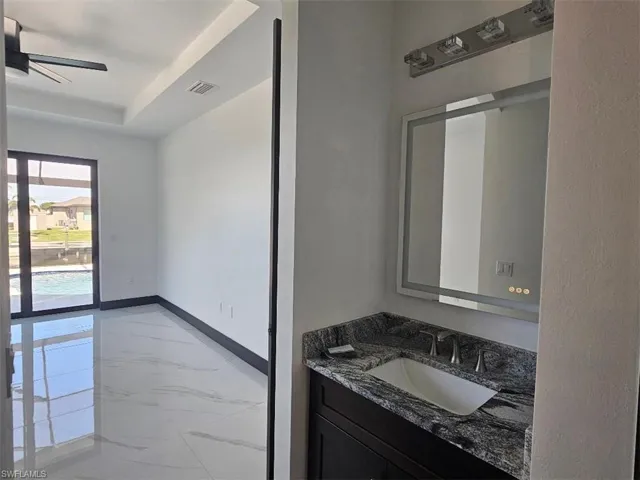 Bathroom featuring marble finish floor, a raised ceiling, a ceiling fan, vanity, and baseboards