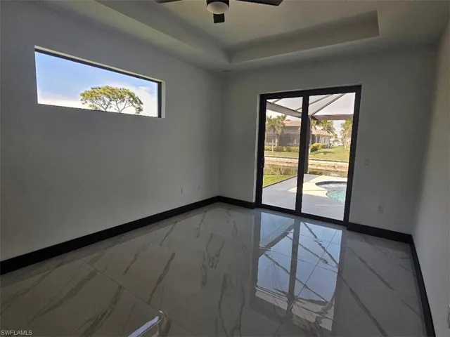 Empty room featuring a raised ceiling, a healthy amount of sunlight, marble finish floor, and baseboards