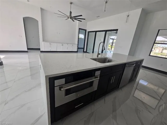 Kitchen featuring a sink, marble finish floor, dark cabinetry, appliances with stainless steel finishes, and a center island with sink