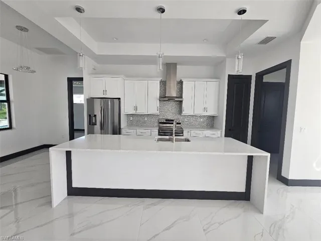 Kitchen featuring a raised ceiling, visible vents, appliances with stainless steel finishes, a sink, and wall chimney range hood