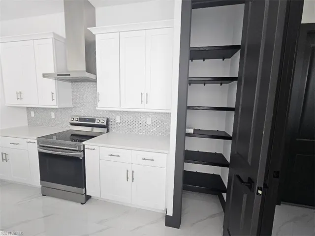 Kitchen with marble finish floor, wall chimney exhaust hood, electric range, and white cabinetry