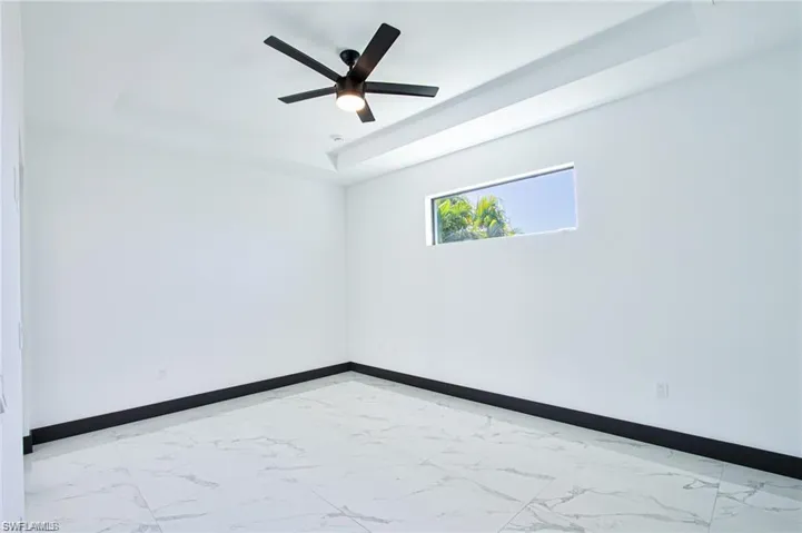 Unfurnished room featuring ceiling fan, marble finish floor, a raised ceiling, and baseboards