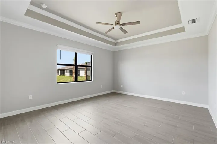 Tray ceiling with crown molding, ceiling fan, large window, tile flooring, and light-toned walls