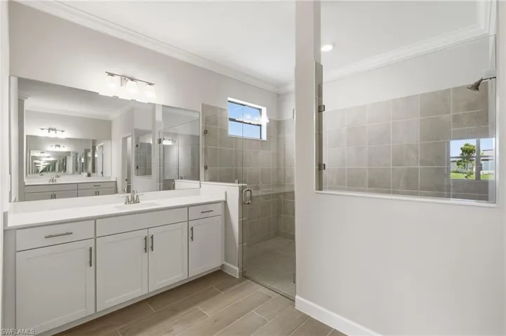 Dual vanity with white cabinetry and integrated sinks, a glass-enclosed shower with tile surround, and a clerestory window