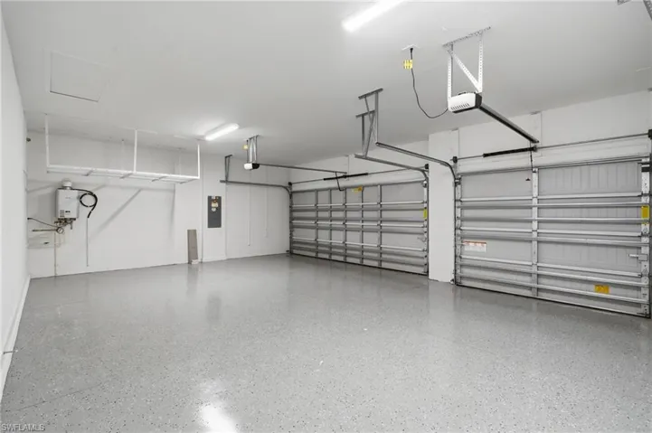 Two overhead garage doors with automatic openers, coated concrete flooring, and a wall-mounted water heater