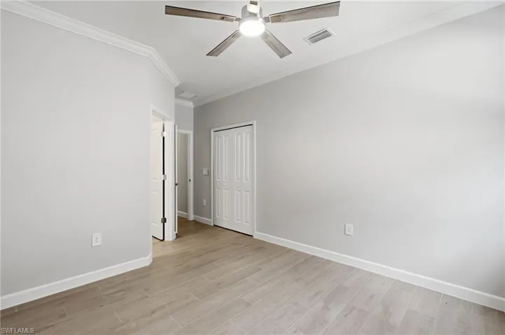 Neutral wall paint, ceiling fan with integrated lighting, wood-finish flooring, white crown molding, and white baseboards