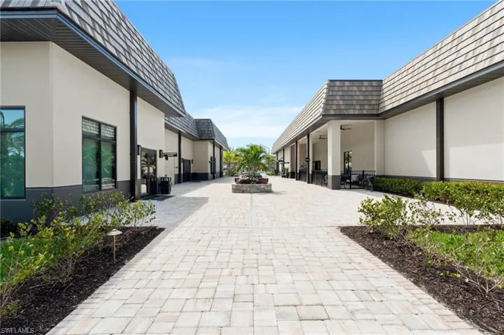Paver walkway with landscape lighting, bordered by structured landscaping, leading to buildings with hip roofs and stucco exteriors