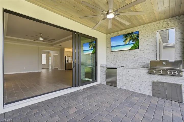 Covered outdoor living space featuring paver flooring, a built-in grill, and ceiling fans