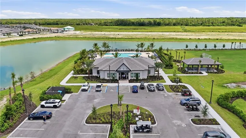 Modern amenity center featuring an outdoor swimming pool, extensive paved parking, covered outdoor lounge, and expansive green spaces