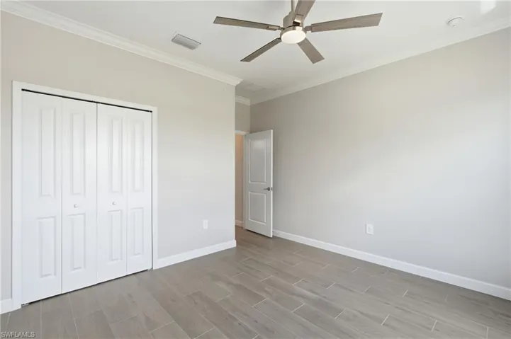 Room featuring wood-look tile flooring, crown molding, a ceiling fan with integrated lighting, and bi-fold closet doors