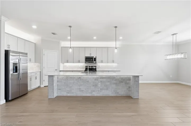 Open-concept kitchen featuring an expansive island with stone veneer, stainless steel appliances, and a tile backsplash
