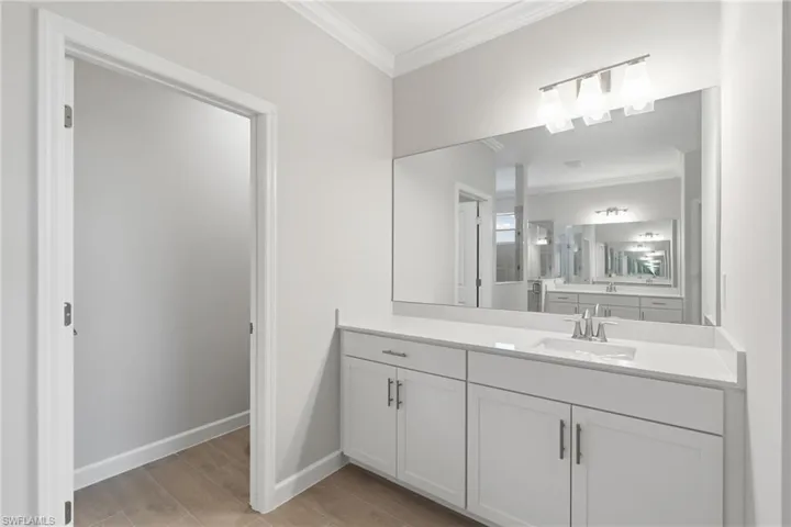 Recessed sink with a chrome faucet, large vanity mirror, three-light vanity fixture, white shaker-style cabinetry, and wood-finish flooring