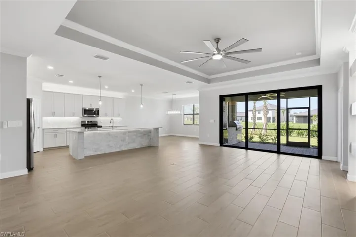 Spacious open-concept interior with wood-finish flooring, recessed lighting, and a tray ceiling with a ceiling fan