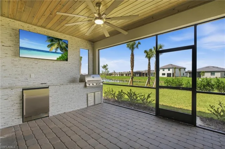 Screened lanai featuring wood-finish ceiling, paver flooring, built-in outdoor kitchen with stainless steel appliances, and ceiling fan
