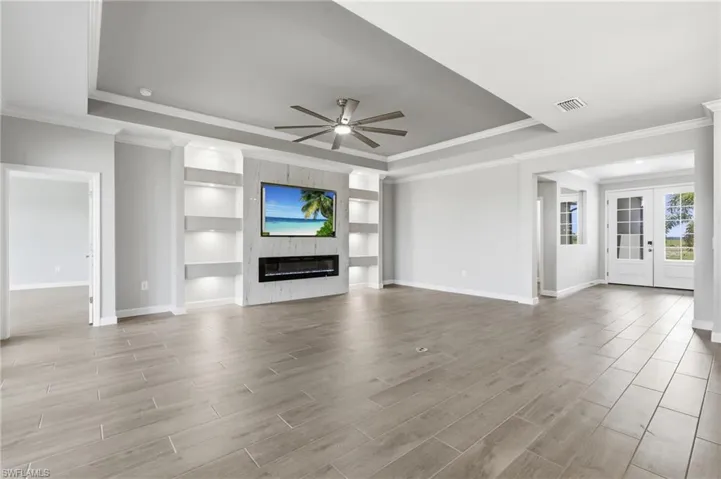 Expansive living space featuring wood-finish flooring, a tray ceiling, and a built-in media center with shelving and an electric fireplace