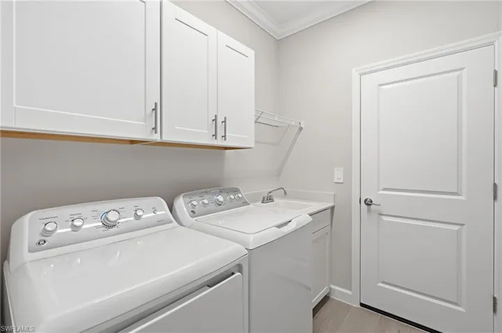 White shaker-style cabinetry, crown molding, utility sink, and wood-finish flooring