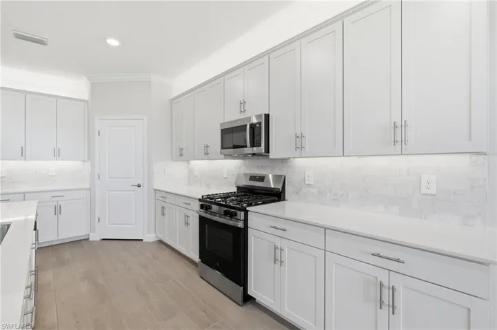 White cabinetry with brushed nickel hardware, stainless steel gas range, built-in microwave, light-toned countertops, and wood-finish flooring