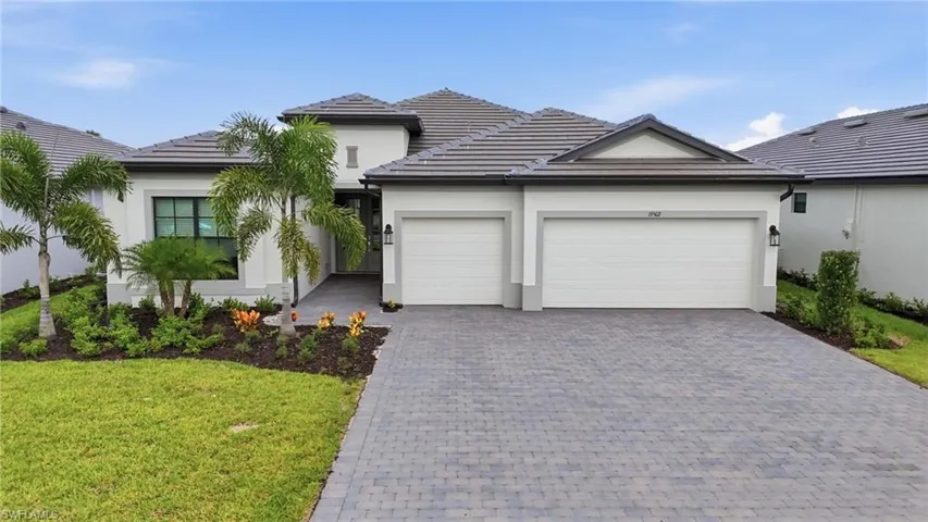 Stucco exterior with a tile roof, paver driveway, and an attached two-car garage