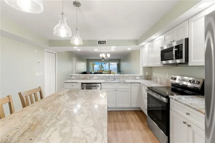 Kitchen featuring stainless steel appliances, decorative light fixtures, white cabinetry, a chandelier, and light wood-style floors