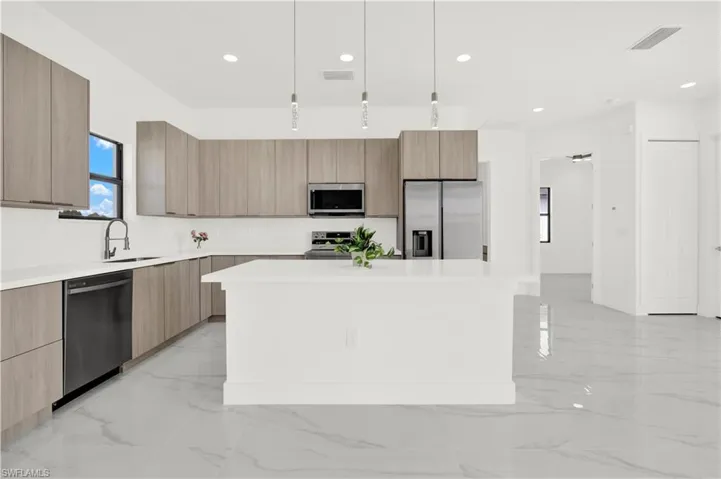 Kitchen featuring modern cabinets, stainless steel appliances, a kitchen island, pendant lighting, and light marble finish floors