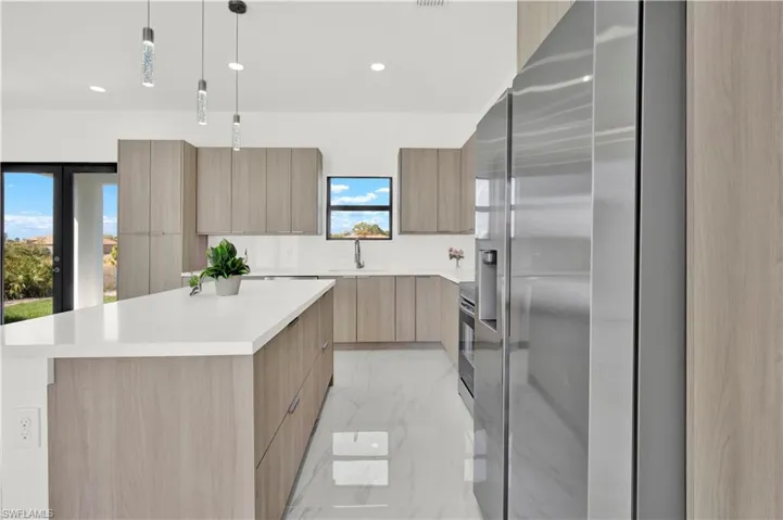 Kitchen featuring a kitchen island, modern cabinets, stainless steel appliances, decorative light fixtures, and light marble finish flooring