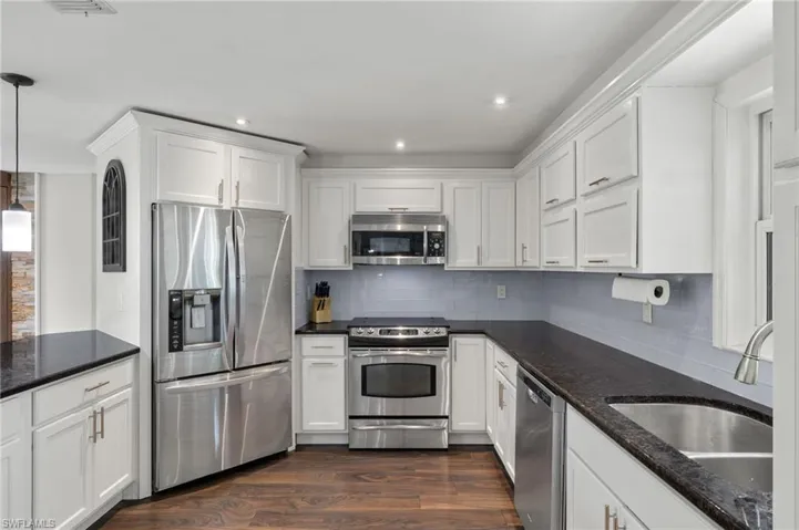 Kitchen with stainless steel appliances, dark stone counters, dark wood-style floors, and white cabinetry