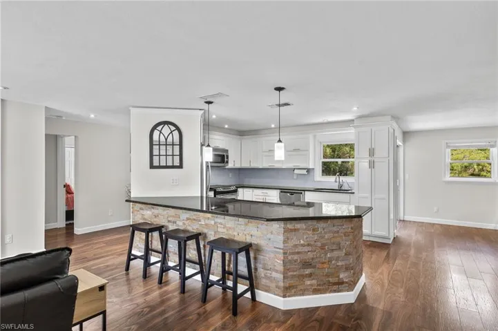 Kitchen with white cabinets, dark wood finished floors, hanging light fixtures, stainless steel appliances, and a breakfast bar