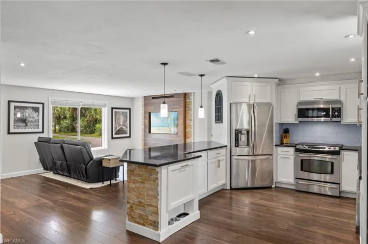 Kitchen with stainless steel appliances, open floor plan, white cabinetry, and decorative backsplash