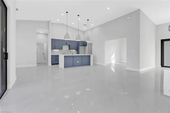 Kitchen with decorative light fixtures, blue cabinetry, backsplash, sink, and high vaulted ceiling