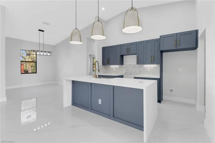 Kitchen with tasteful backsplash, sink, a high ceiling, hanging light fixtures, and a kitchen island with sink