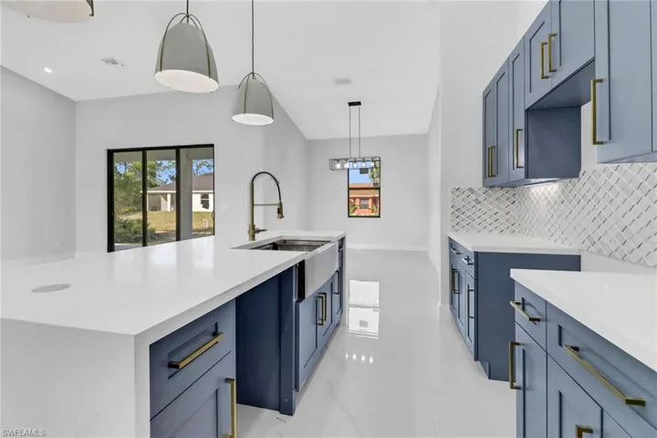 Kitchen with backsplash, pendant lighting, sink, a kitchen island with sink, and blue cabinets
