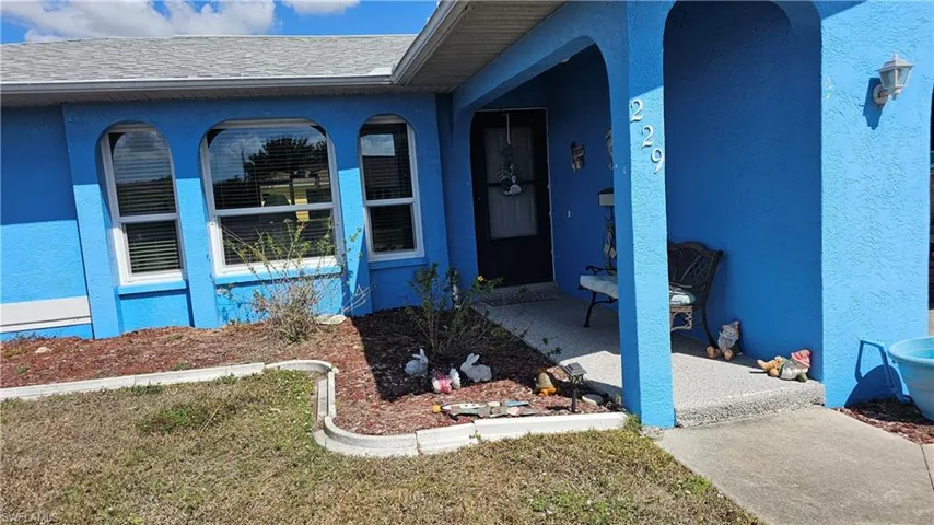 Property entrance with stucco siding, roof with shingles, and a yard