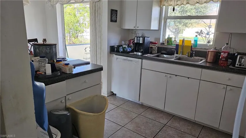 Kitchen with dark countertops, dishwashing machine, white cabinets, and light tile patterned floors