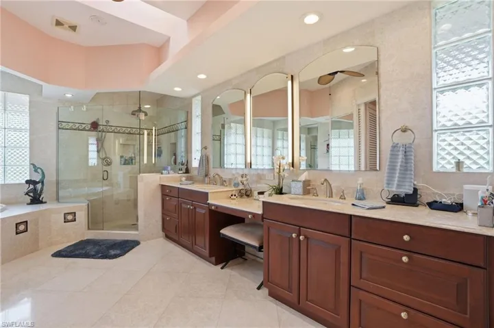 Bathroom featuring two vanities, a shower stall, a bath, light tile patterned floors, and ceiling fan