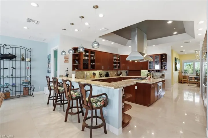 Kitchen featuring open shelves, glass fronted cabinets, a kitchen breakfast bar, a peninsula, and island exhaust hood
