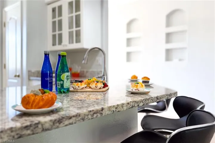 Kitchen view of light stone countertops, glass insert cabinets, a kitchen bar, and white cabinetry