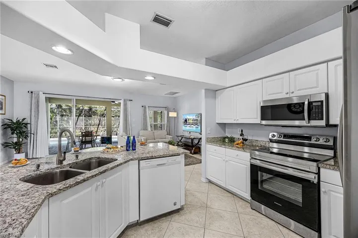 Kitchen featuring stainless steel appliances, white cabinets, light stone countertops, open floor plan, and recessed lighting