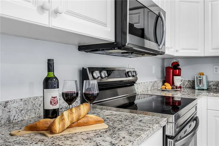 Kitchen featuring stainless steel appliances, white cabinets, and light stone countertops