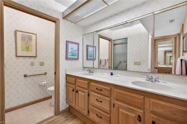 Full bathroom with wallpapered walls, double vanity, a shower with shower door, and light wood-style flooring