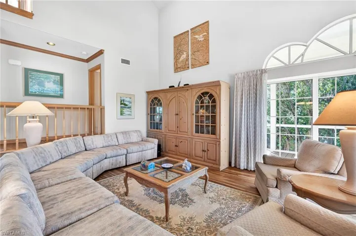 Living room with a high ceiling, plenty of natural light, wood finished floors, and ornamental molding