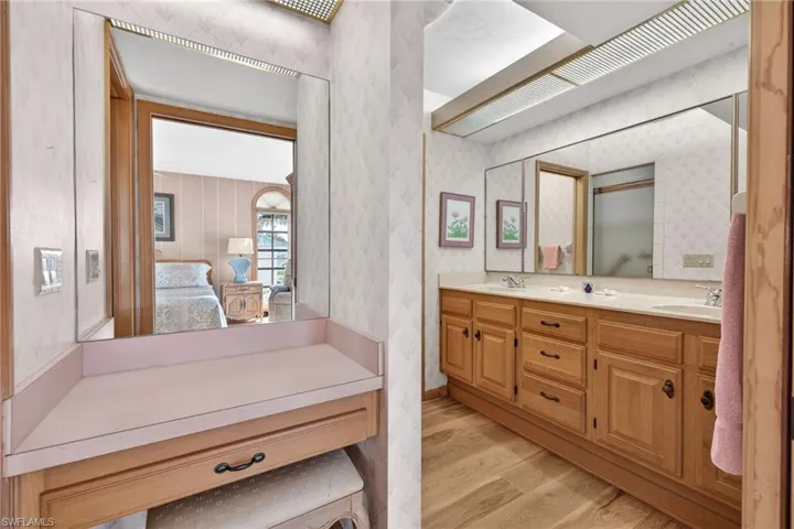 Ensuite bathroom with double vanity, light wood finished floors, and wallpapered walls