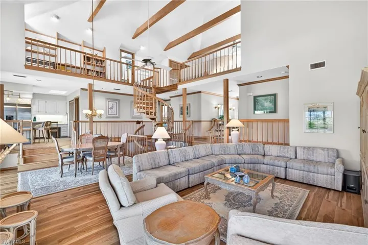 Living area featuring high vaulted ceiling, wood-type flooring, a ceiling fan, a wainscoted wall, and plenty of natural light