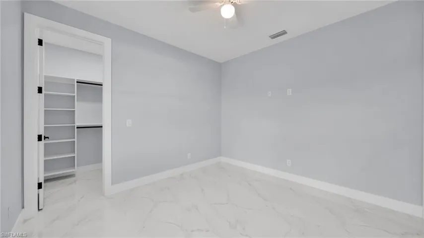 Unfurnished bedroom featuring light marble finish floors, a spacious closet, and a ceiling fan