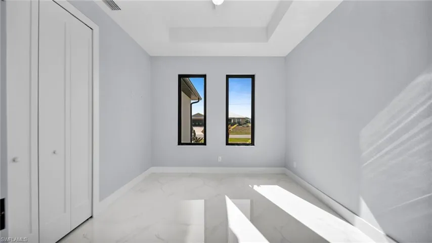 Unfurnished bedroom featuring light marble finish floors, a raised ceiling, and a closet