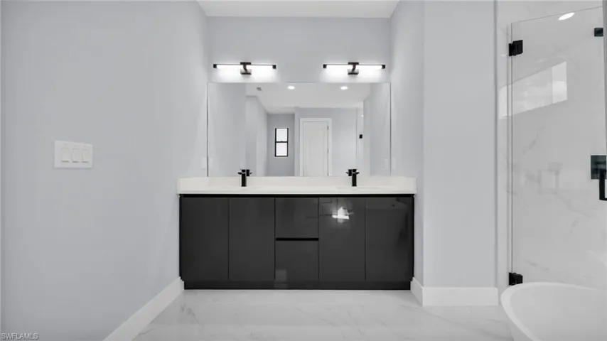 Full bath featuring light marble finish floors, a marble finish shower, and double vanity